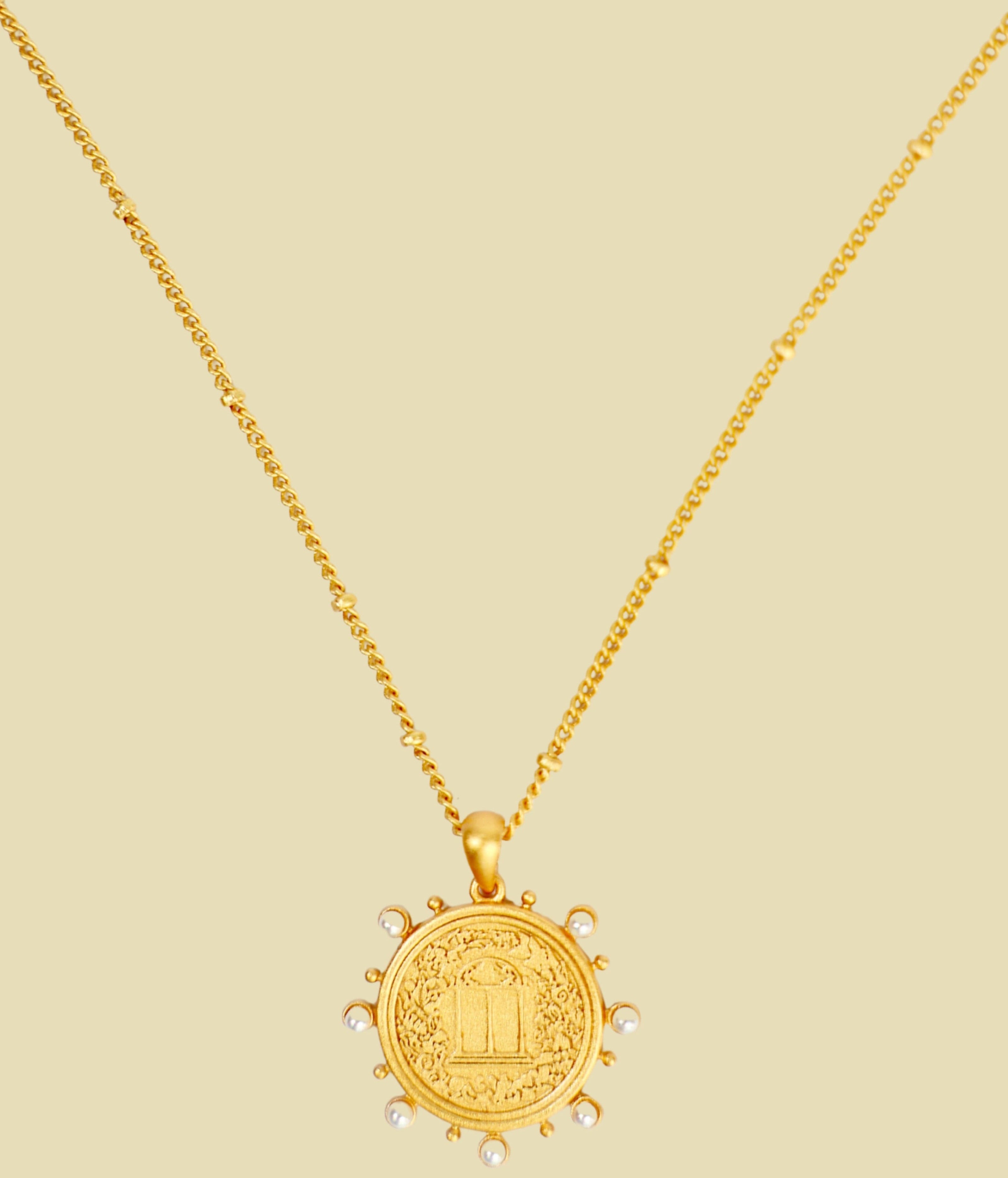 Gold necklace with a round coin pendant on a beige background
