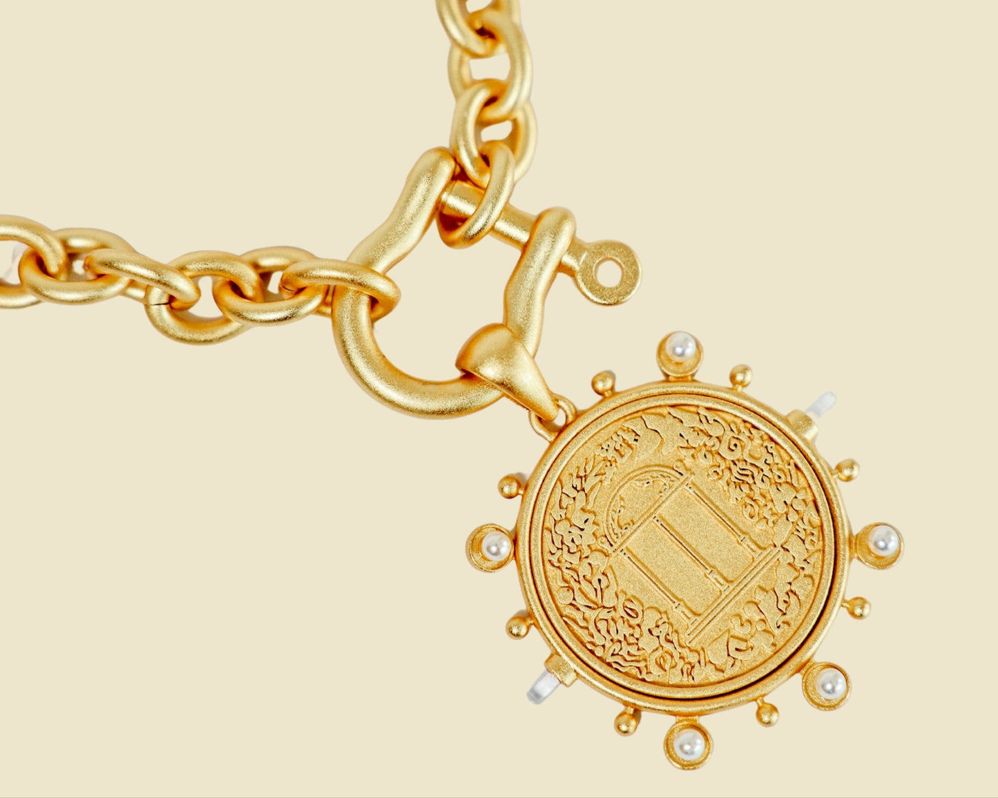 Gold necklace with a detailed coin charm on a beige background