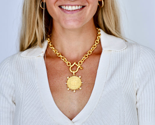 Woman wearing a gold chain necklace with a pendant against a white background