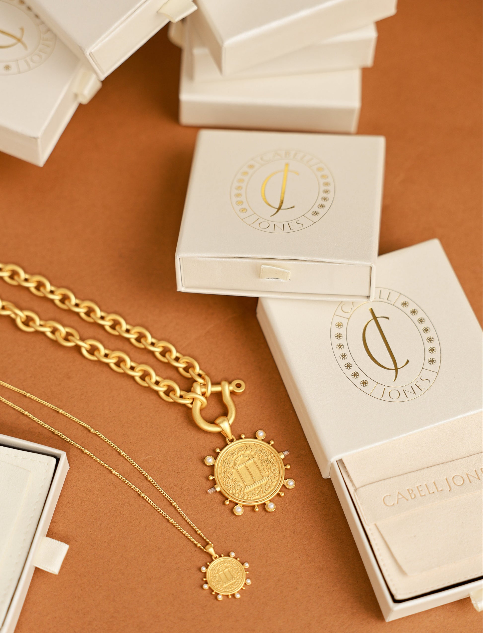 Gold necklace with pendant on a brown surface with white boxes.